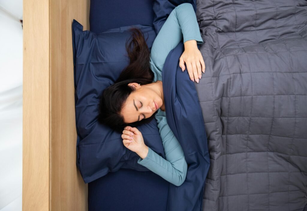 A woman peacefully sleeping under a cozy, dark blue bedding set in a serene bedroom environment.
